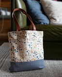 Floral-patterned tote bag with a dark blue base on a carpeted floor.