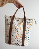 Floral-patterned tote bag with brown straps held by a person against a neutral background
